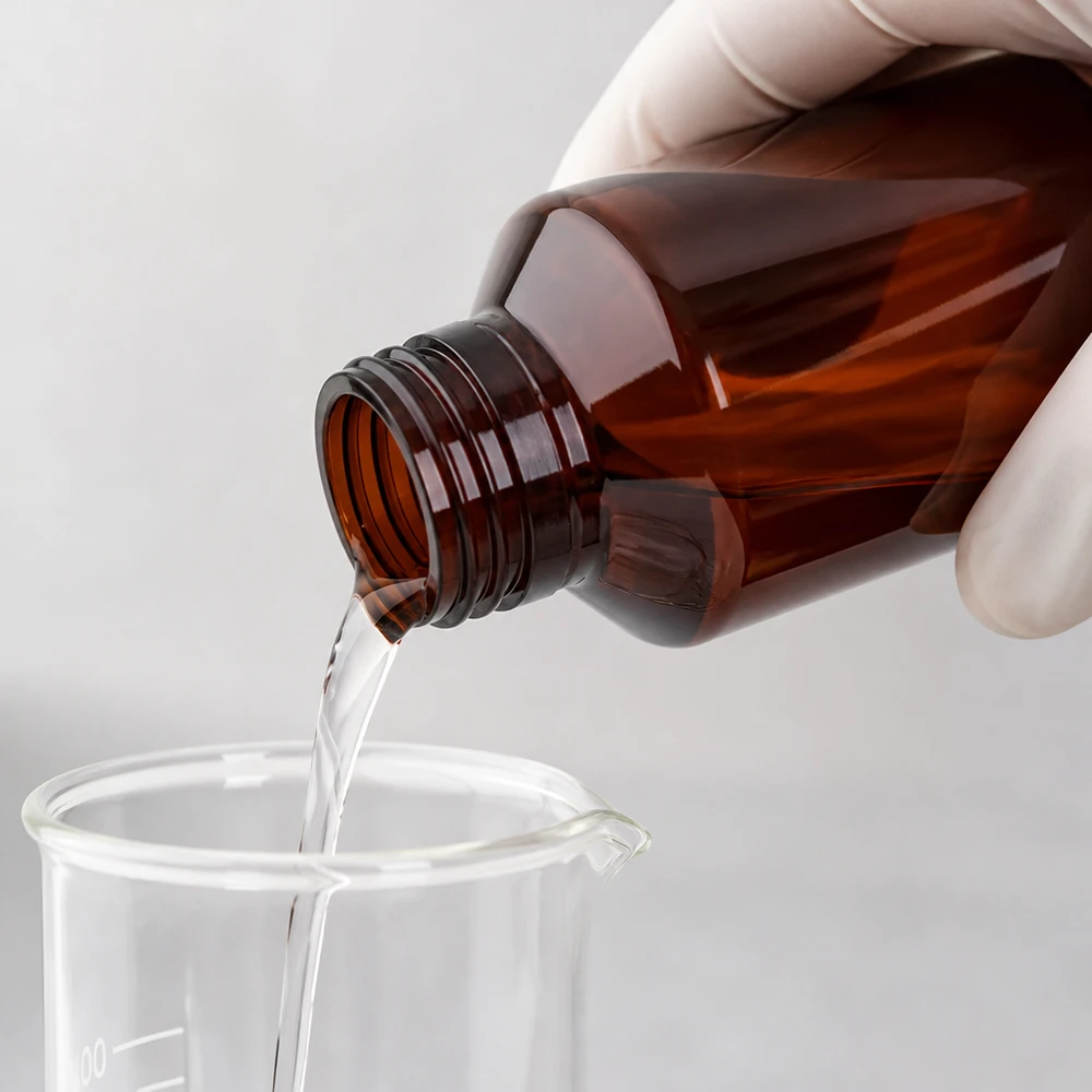 PET láhev 100ml se zeleným uzávěrem s ochranou proti manipulaci Čirá tekutina se nalévá z hnědé 100ml PET láhve do skleněné nádoby
