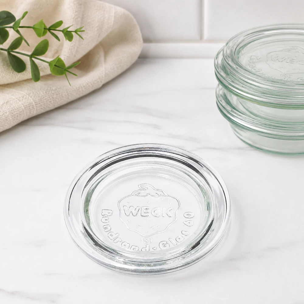 WECK Glasdeckel RR60 Stapelansicht mehrere Deckel übereinander auf Marmor mit Küchenhandtuch und grünem Zweig