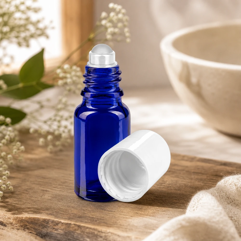 Lékárenská lahvička modrá 10ml roll-on uzávěr bílý Blaue 10ml Apothekerglasflasche mit Rollapplikator neben Keramikschale und Naturblüten