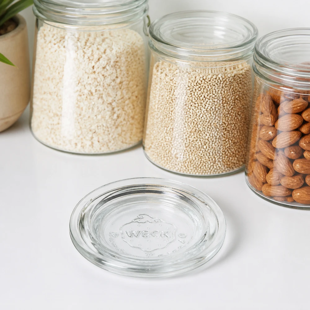 Skleněné víčko WECK RR40 WECK Glasdeckel RR40 transparent vor Vorratsgläsern mit Reis Quinoa und Nüssen auf weißer Arbeitsplatte