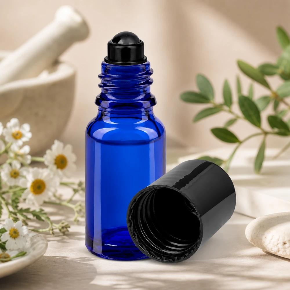 Kleine blaue 10ml Rollerflasche aus Apothekerglas neben weißen Blüten und grünen Zweigen
