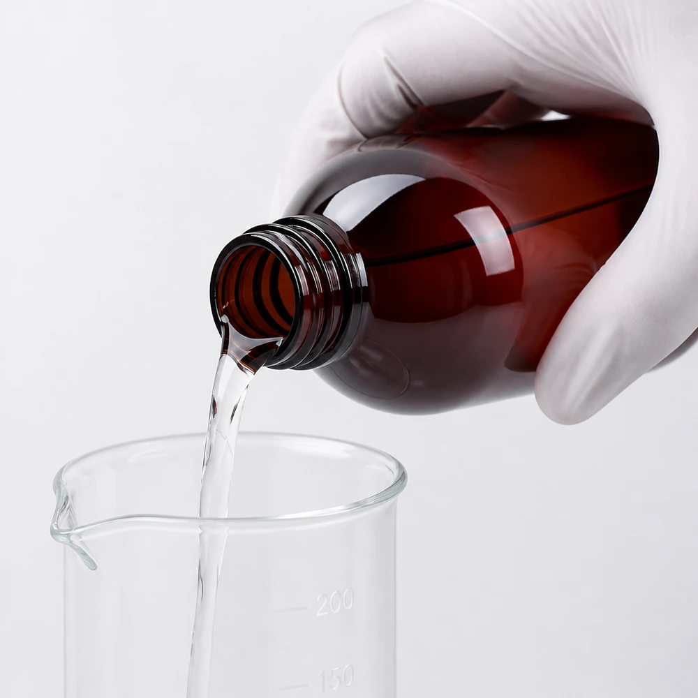 Hnědá PET láhev o objemu 250 ml se pomocí ochranných rukavic vylije do laboratorní odměrky