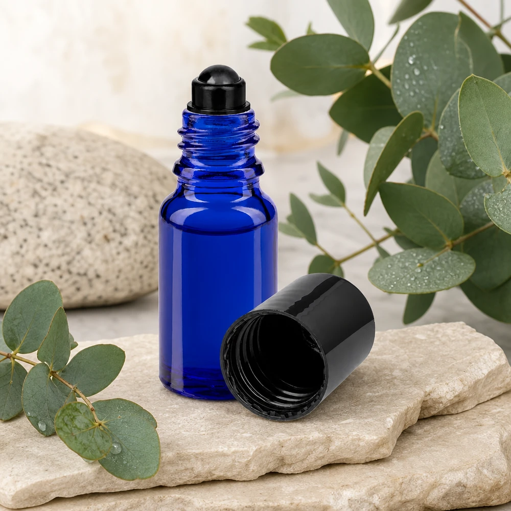 Lékárenská lahvička modrá 10ml roll-on černá uzávěr Blaue 10ml Rollerflasche aus ApoGlas mit schwarzer Rollkugel auf Naturstein vor botanischem Hintergrund