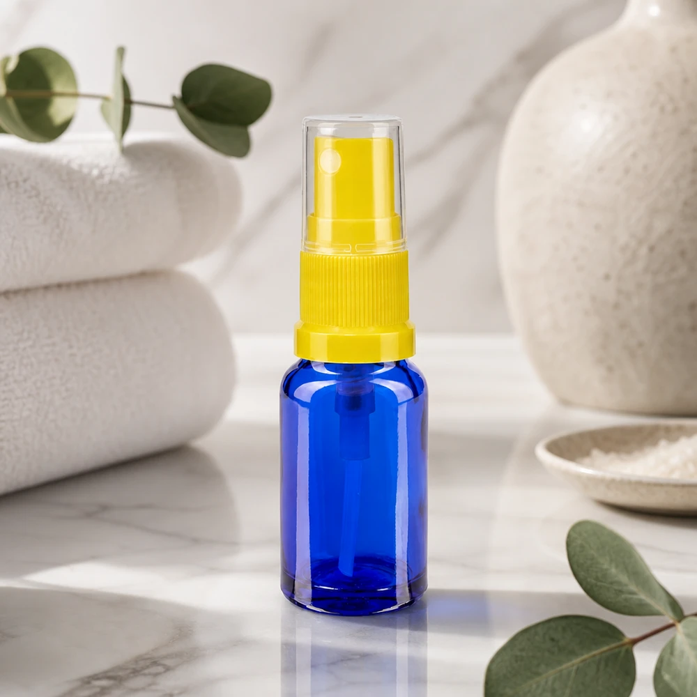 Zylindrische blaue Glassprayflasche 30ml ApoGlas mit gelbem Sprühkopf auf weißem Marmor