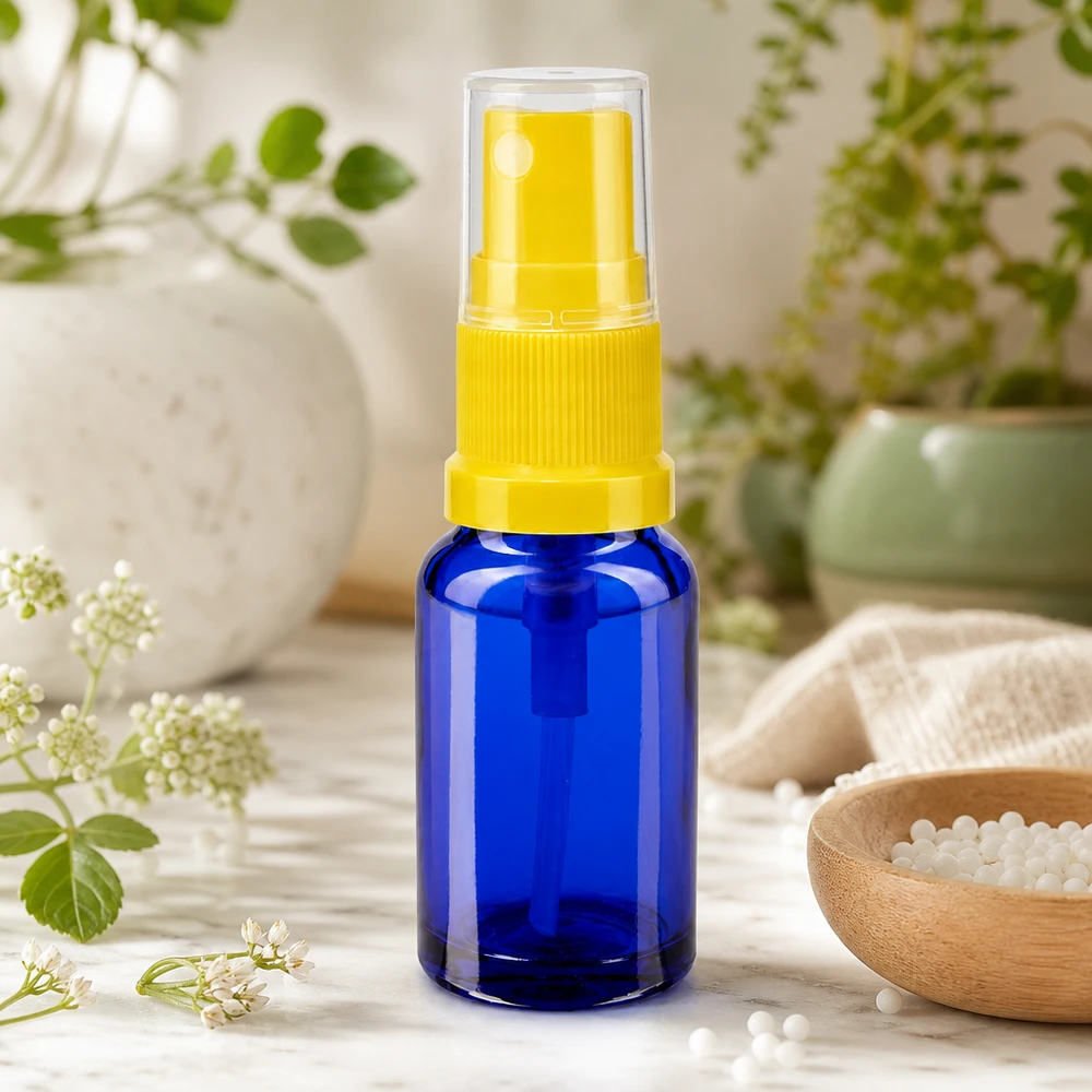 Schlanke Blauglas-Flasche 30ml mit gelbem Zerstäuber neben Homöopathie-Globuli