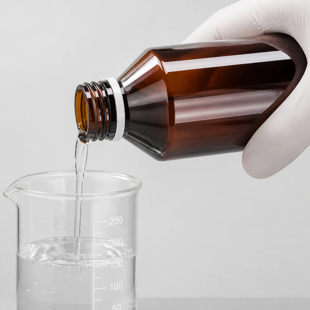 Hnědá PET láhev o objemu 100 ml je vyprázdněna do kádinky, s bílým rýhovaným uzávěrem zaručujícím neporušenost