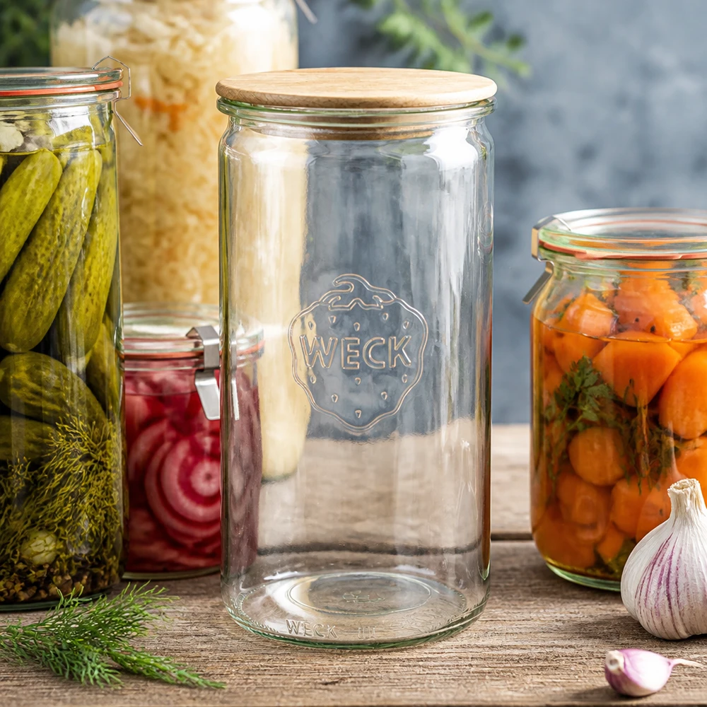 1590ml válcová sklenice WECK RR100 s dřevěným víkem buk. WECK Zylinderglas 1590ml RR100 mit Holzdeckel zwischen Einmachgläsern mit Gurken Karotten und Sauerkraut auf Holztisch