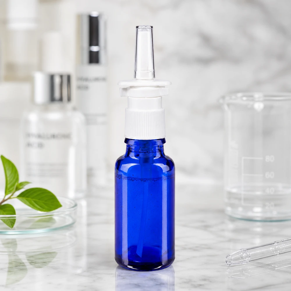 Lékárenská lahvička modrá 20ml nosní rozprašovač bílá stř. Arzneimittelflasche 20ml in Blauglas mit Nasenzerstäuber und transparentem Applikator auf Marmorfläche