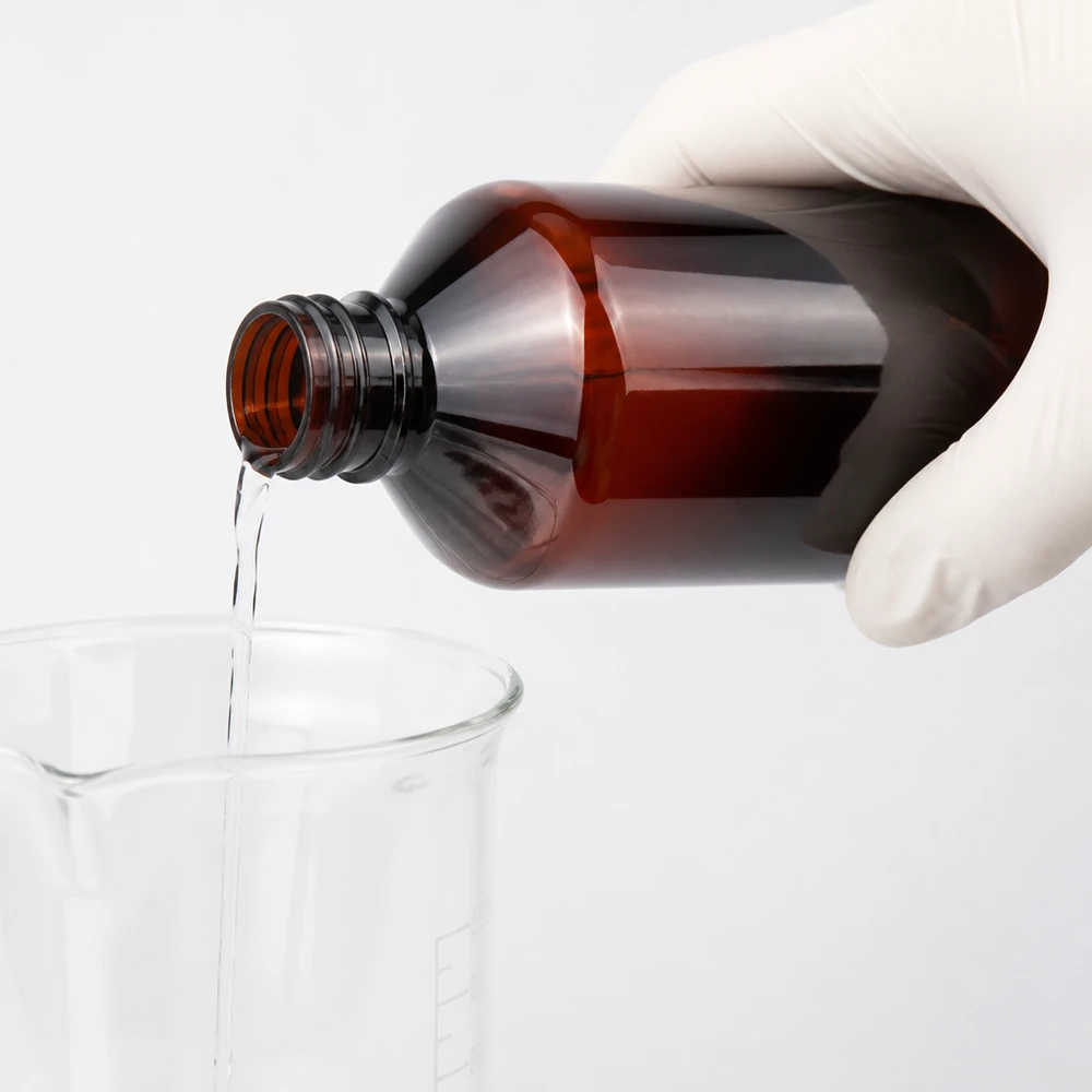 PET láhev 1000ml se standardním bílým uzávěrem s pojistkou proti manipulaci Chemikálie se nalévá z hnědé 1litrové PET láhve do kádinky, přičemž se používají ochranné rukavice
