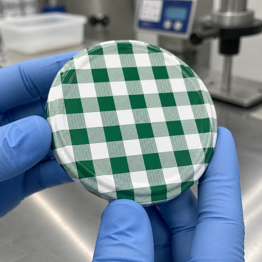 Detailní záběr na šroubovací uzávěr BasicSeal 82 mm TO82 se zeleno-bílým kostkovaným vzorem v laboratorních rukavicích