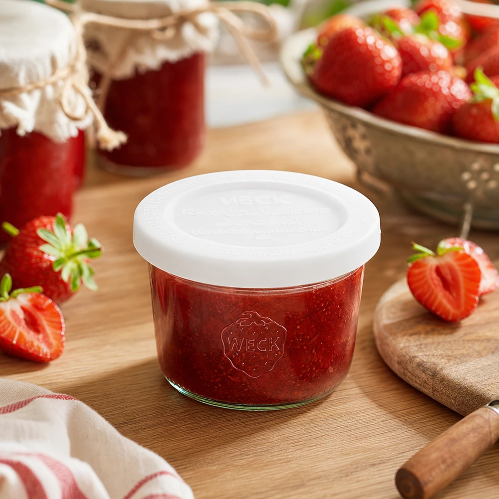 WECK 80ml Sturzglas RR60 mit Erdbeermarmelade gefüllt auf Holzbrett umgeben von frischen Erdbeeren und Marmeladengläsern