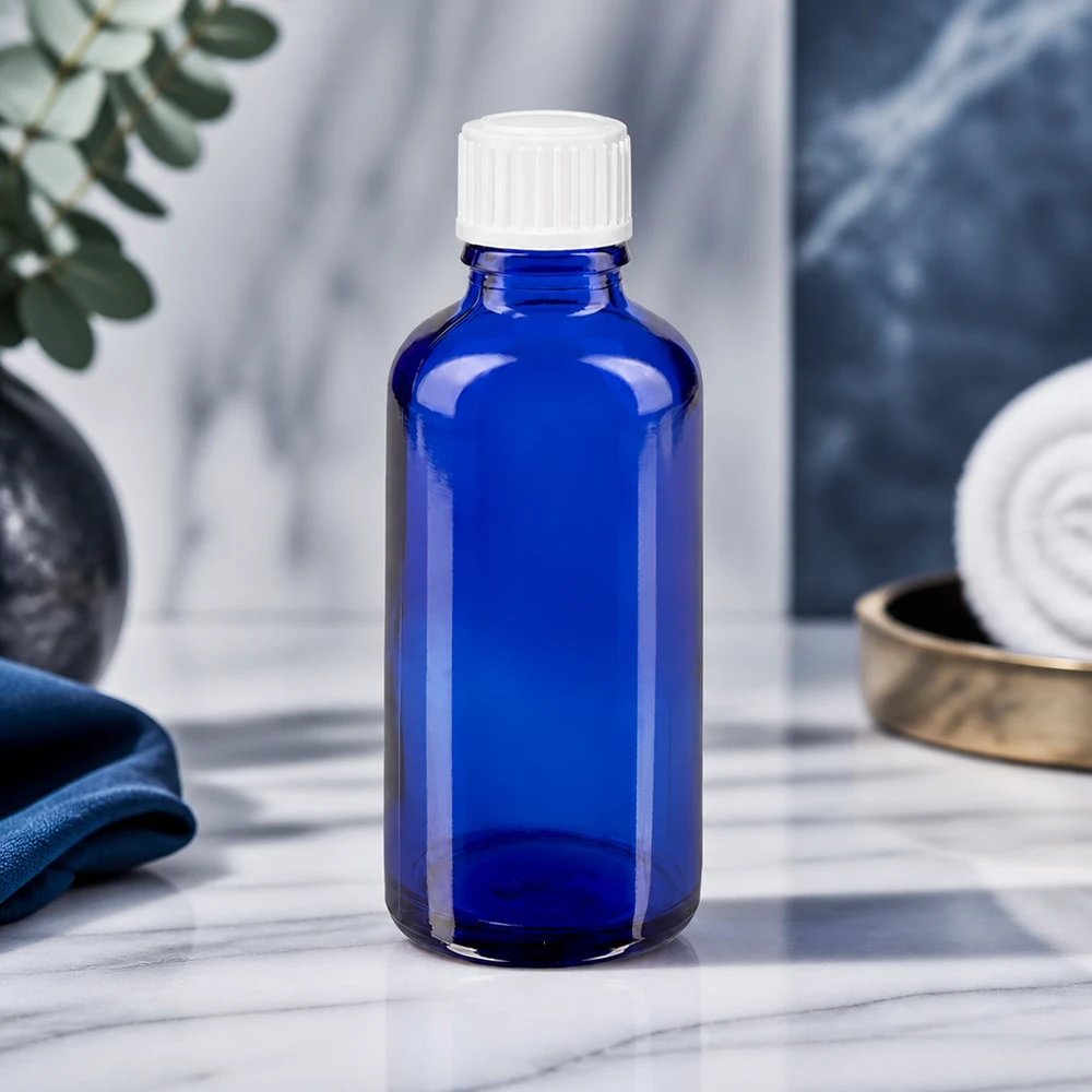 Blaue 50ml Rundflasche ApoGlas mit gerilltem weißen Verschluss vor elegantem Marmor-Hintergrund