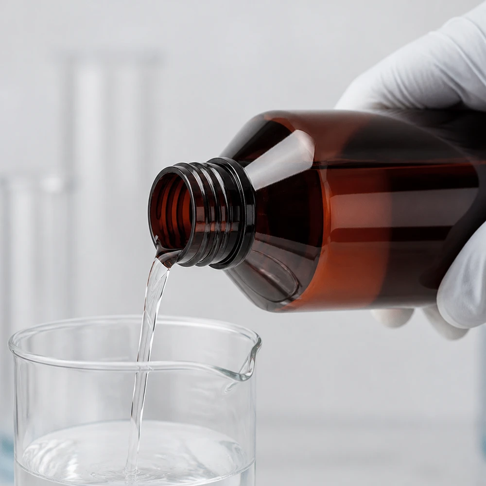 PET láhev 750ml se zeleným uzávěrem prokazatelným proti manipulaci. Laborant v bílých rukavicích nalévá čirou kapalinu z hnědé 750ml PET láhve do kádinky